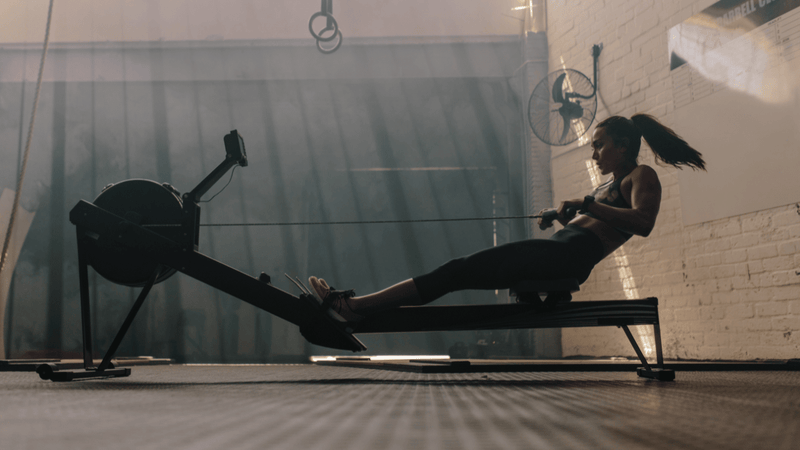 Female athlete performing high-intensity rowing intervals on an indoor rowing machine during repeated effort training in a gym environment.