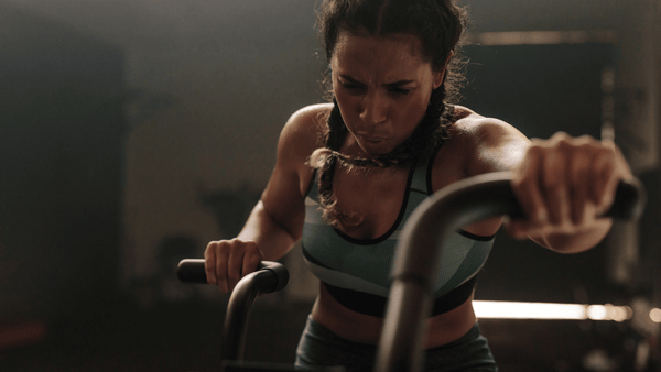 Female athlete pushing hard on an assault bike during high-intensity interval training, illustrating fatigue, cardiovascular strain and repeated efforts.