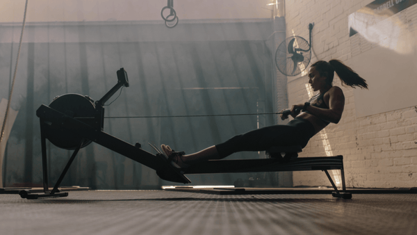 Female athlete performing high-intensity rowing intervals on an indoor rowing machine during repeated effort training in a gym environment.