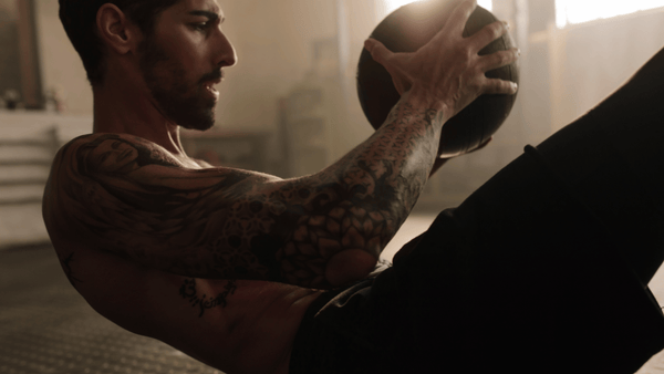 Male athlete performing weighted core training with a medicine ball during high-intensity functional fitness training in a gym environment.
