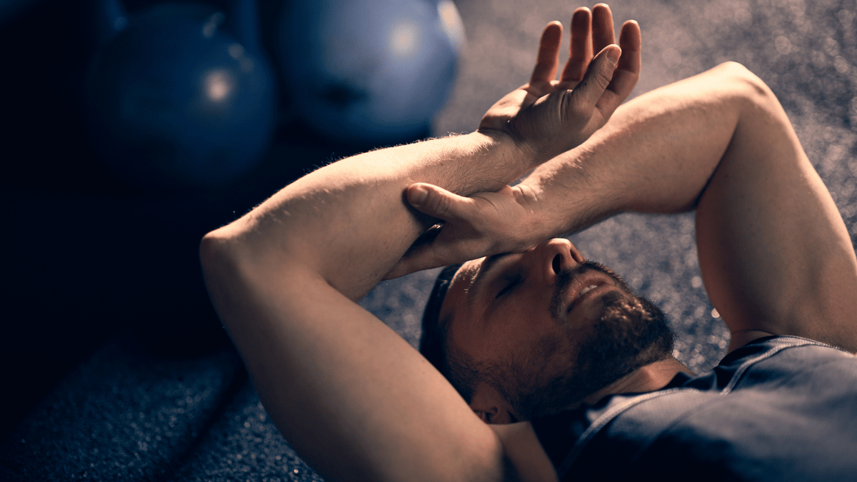 Exhausted male athlete lying on the gym floor recovering after high-intensity training, illustrating fatigue, heat accumulation and recovery between efforts.