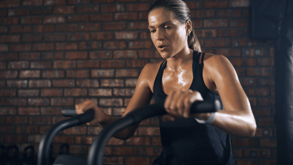 Female athlete covered in sweat during an intense assault bike workout, illustrating heat accumulation and repeated high-output training.