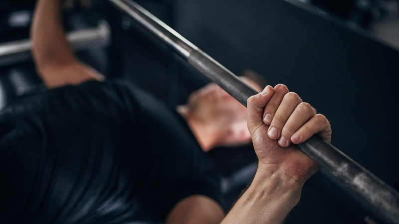 Athlete's hand gripping a loaded barbell mid-set, palm and forearm in close view