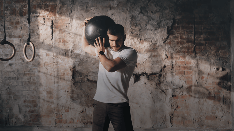 Male athlete performing medicine ball training in a gym environment during functional fitness and repeated high-intensity efforts.